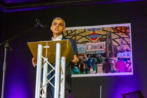 Sir Sadiq Khan speaking on stage at the new Tooting Family Hub in front of a colourful mural showcasing what makes Tooting so special